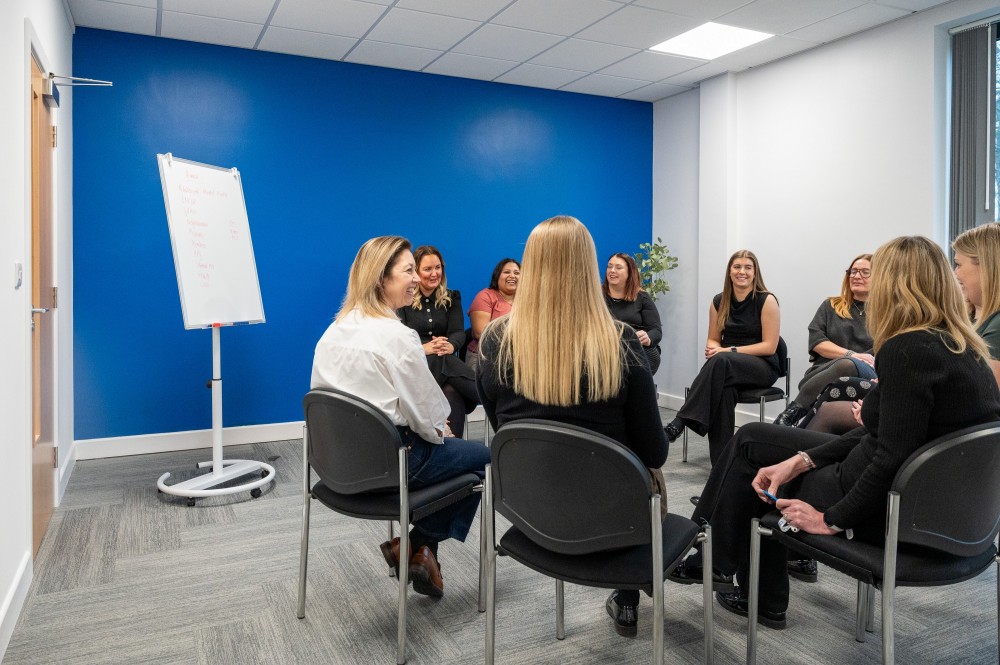 Nine women sat in a circle having a meeting on chairs